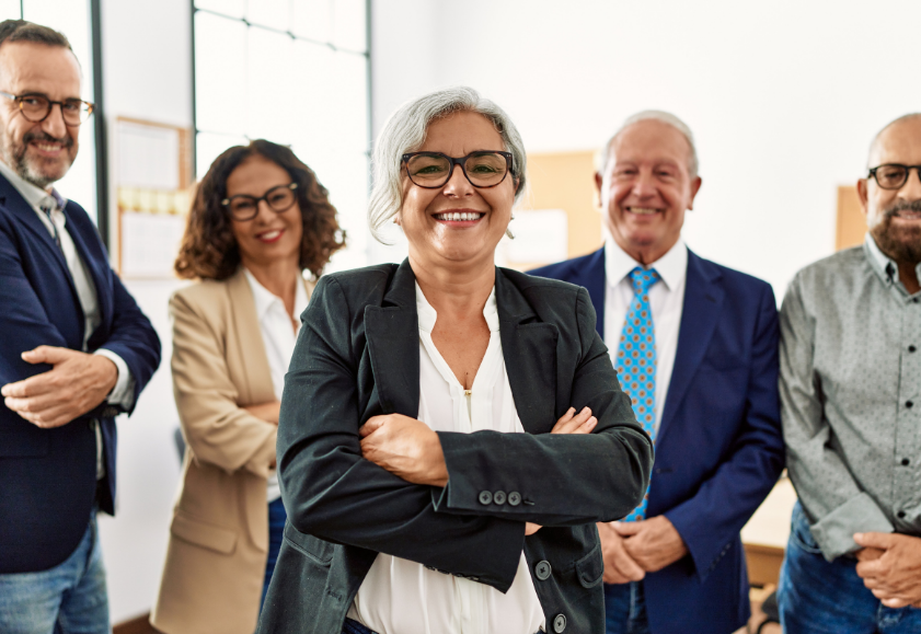 Group of older generation works smiling proudly as they stand in an inclusive office