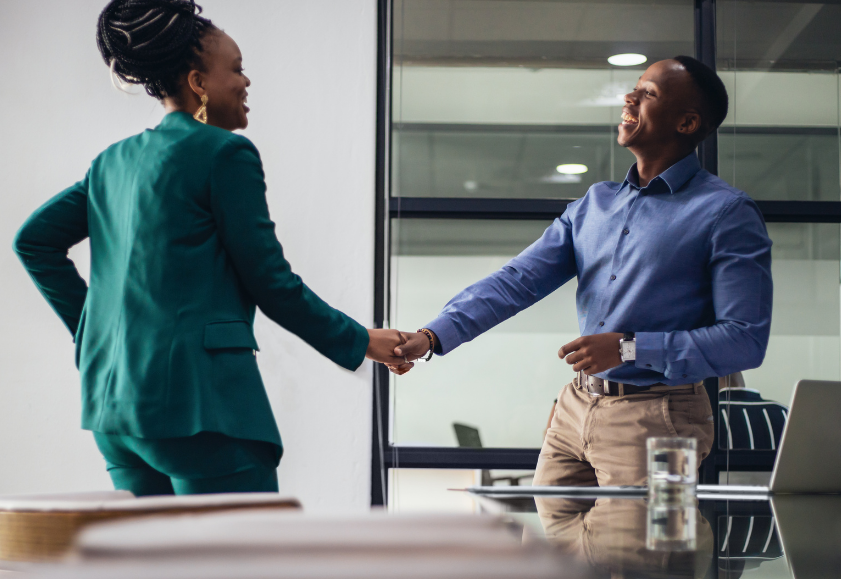 A HR professional and an employee shaking hands and smiling in an office