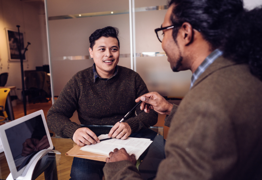 Two professionals in a friendly discussion over a contract, smiling and holding their pens.