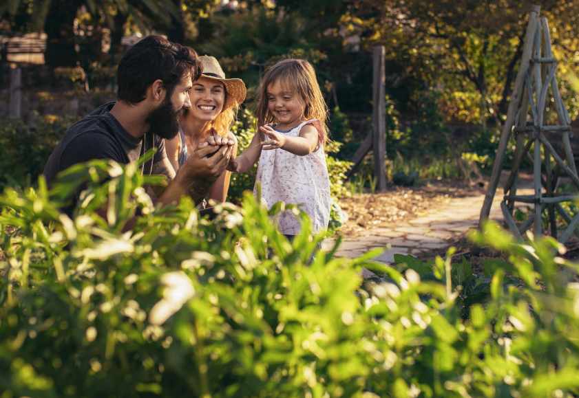 Two parents on leave, smiling, and playing in their garden with their young child