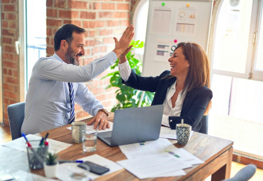 Two mature professionals giving each other a high-five in front of their fixed-term contract and open laptop computer