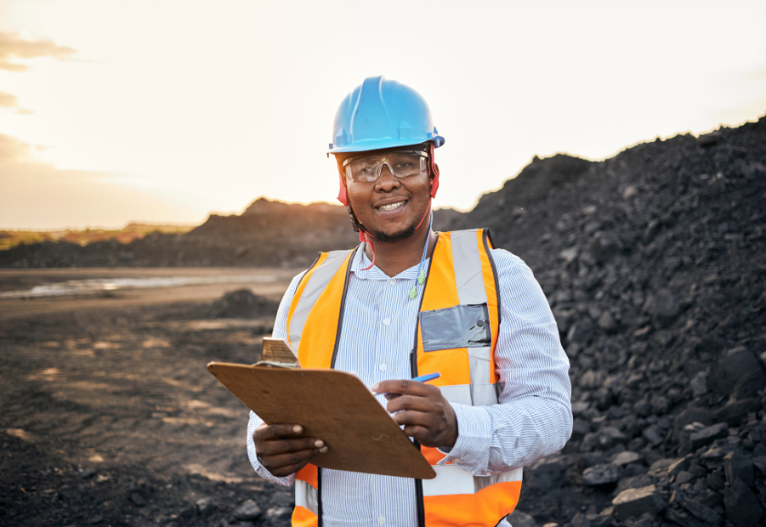 Smiling coal worker with a clipboard standing in front of a pile of coal